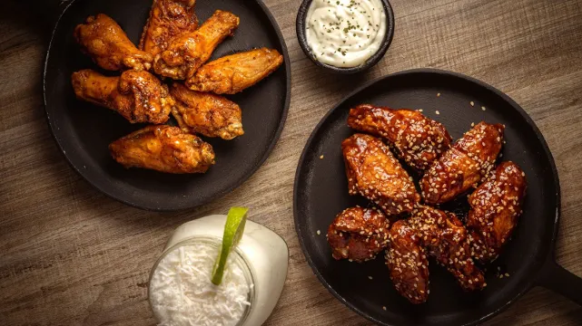 Dos sartenes de alitas glaseadas de Texas BBQ con salsas
